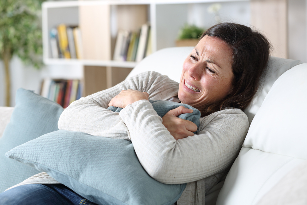 Sad adult woman crying on the sofa, holding pillow