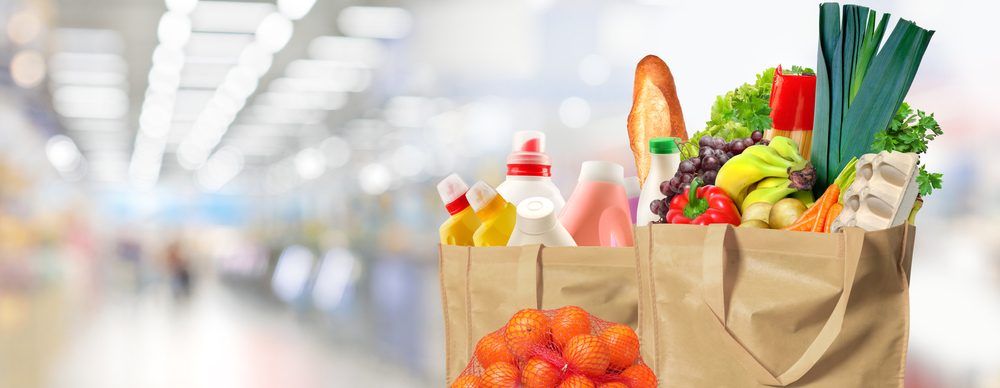 Two ecofriendly reusable grocery shopping bags filled with bread fruits, vegetables, milk and household supplies