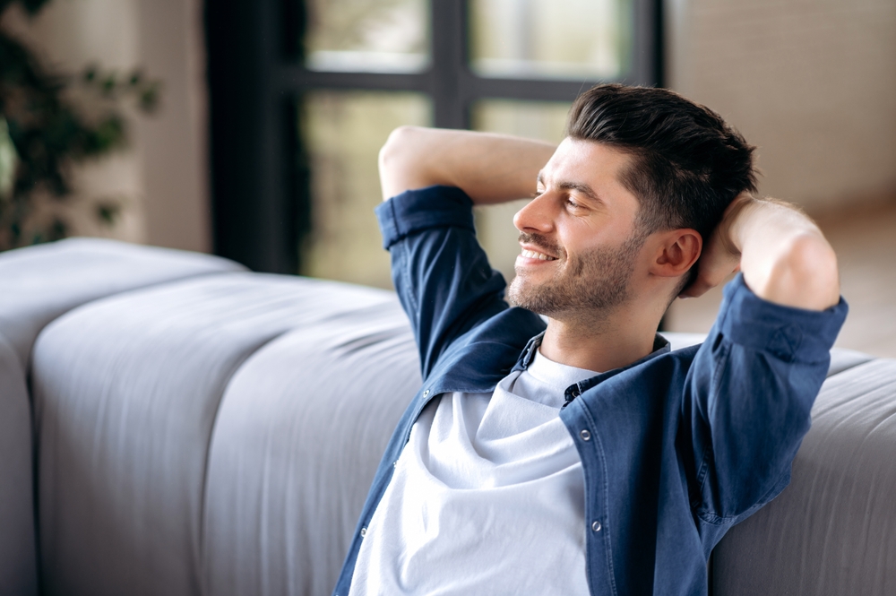 A happy young man sitting on the sofa with both hands on his head, looking very relieved