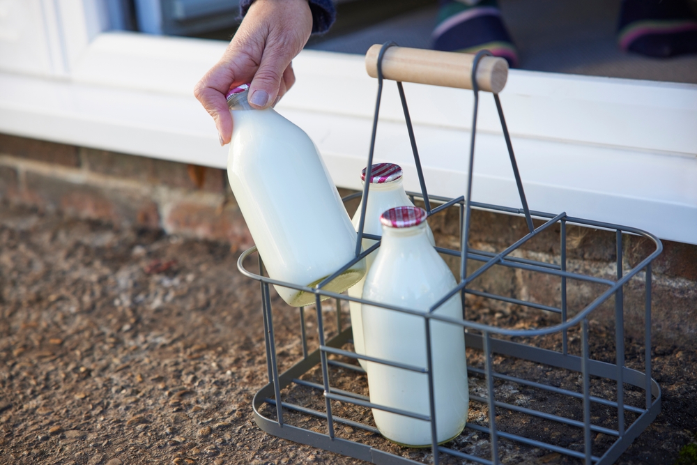 A handing picking up a glass milk bottle from other milk bottles on the doorstep of the house