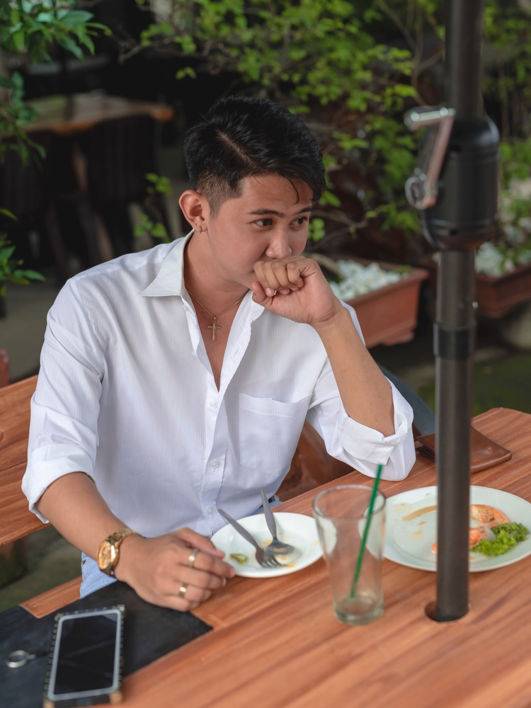 A young Asian man burping after eating at a restaurant