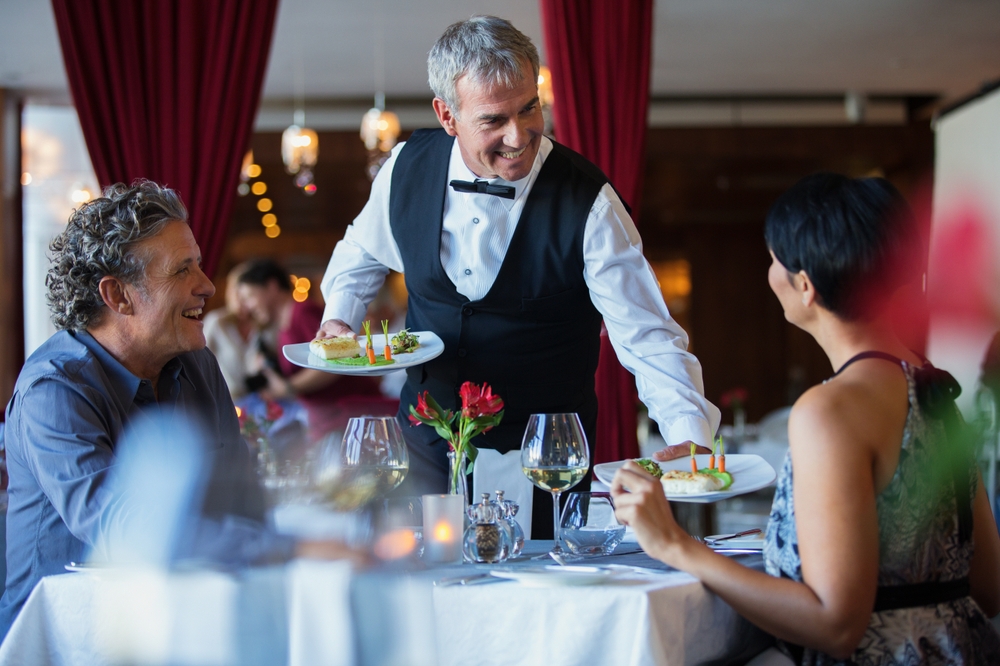 Smiling waiter serving seniors in a luxury formal dining setting