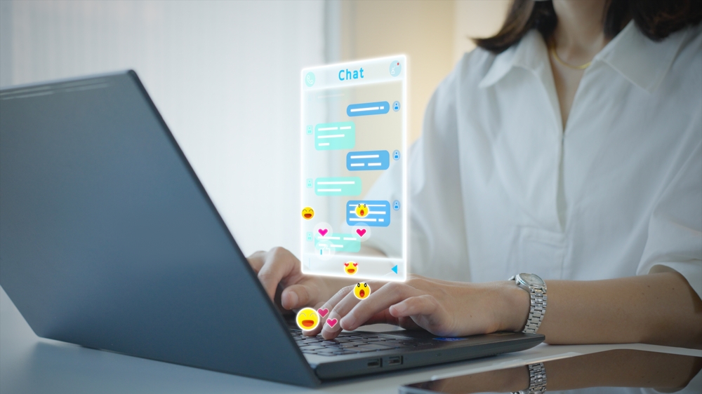 A person sending messages on a laptop and using emojis