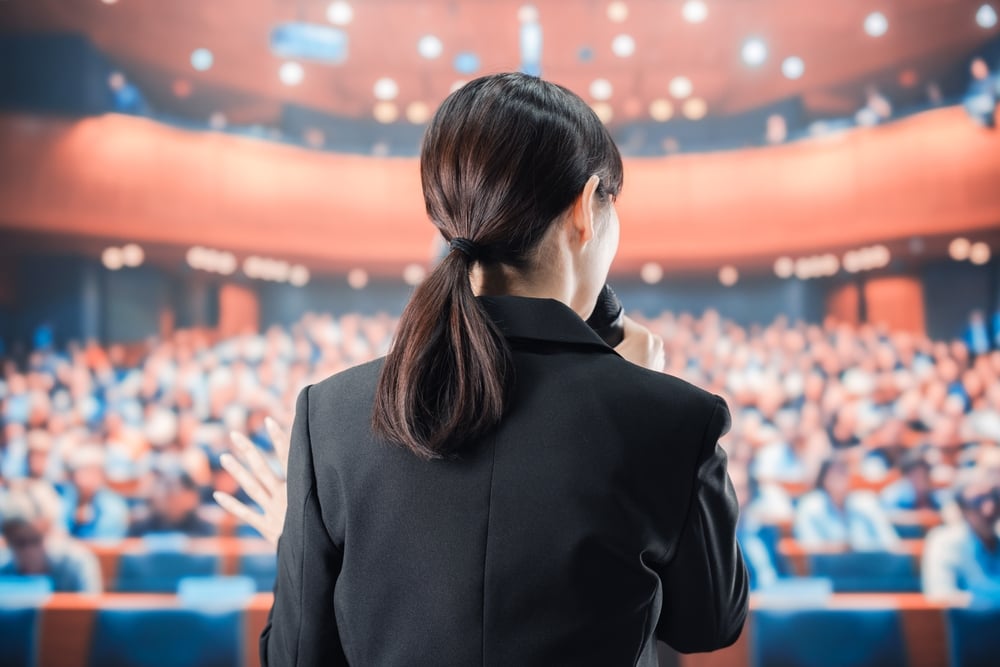 A woman giving a speech in front of a large crowd