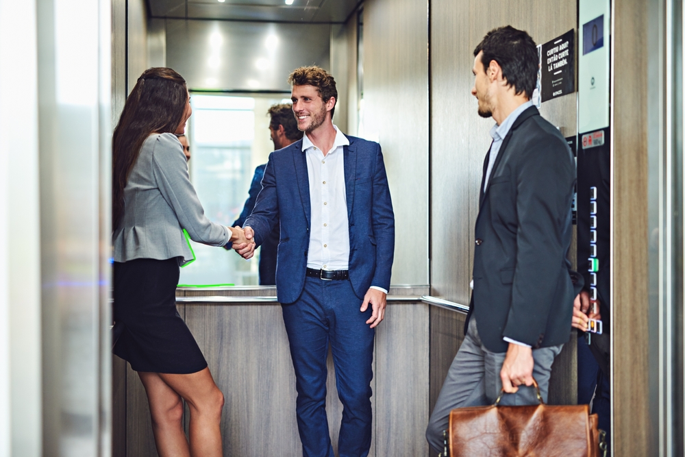Three busines people in an elevator, two of them are shaking hands