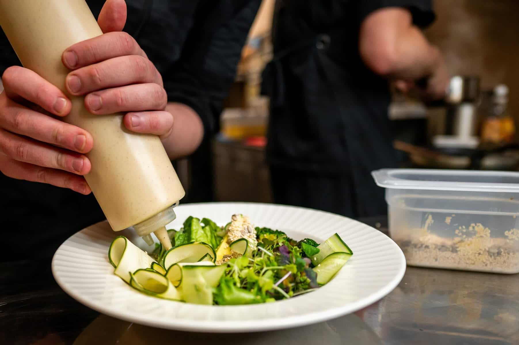 A plate of salad is being garnished with salad dressing by a man