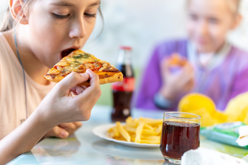 Two young children eating unhealthy snacks and junk food