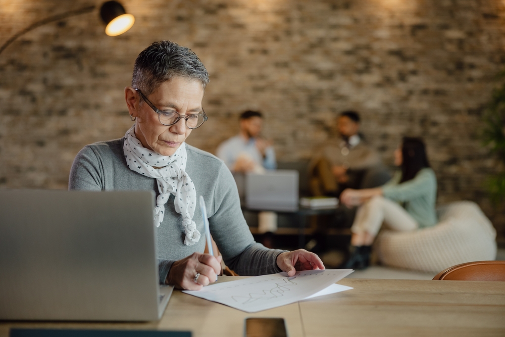 A mature older woman working on some documents with her laptop in a cafe