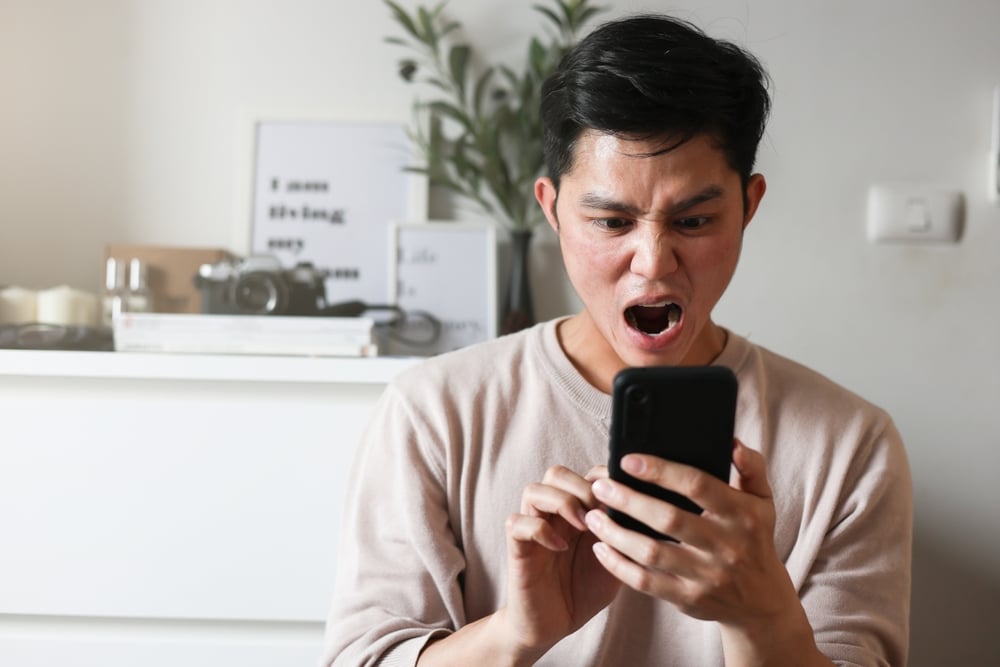 A young Asian man angry with what he sees on his phone