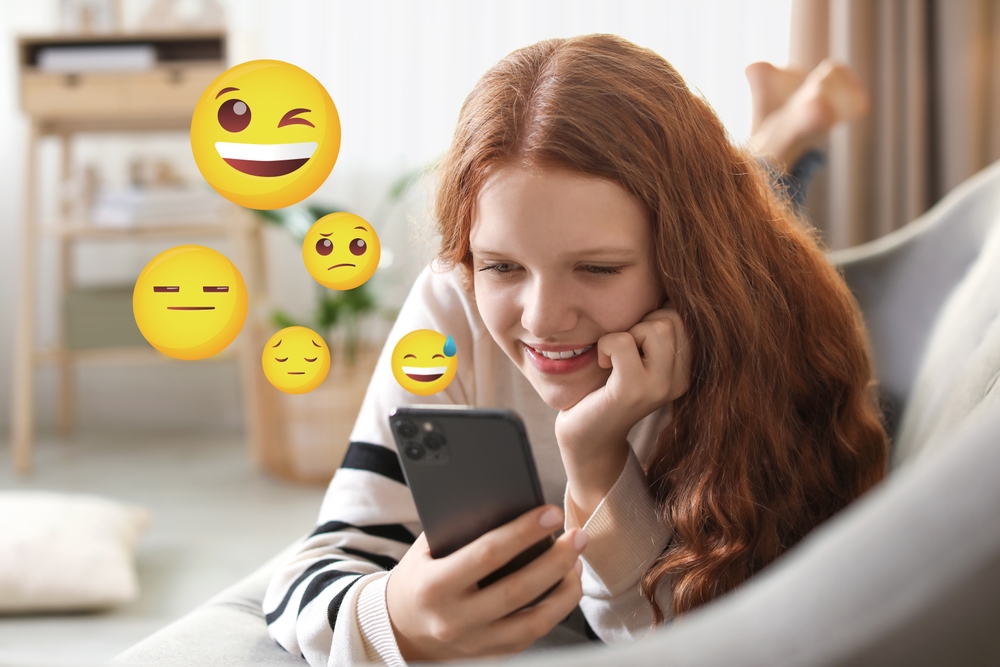 A young woman lying in bed and chatting with emojis on social media
