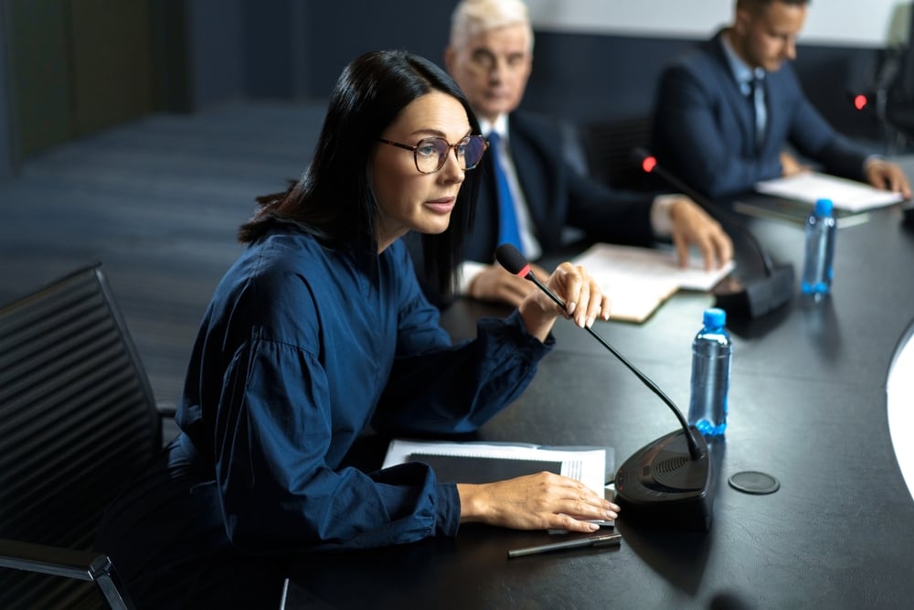 Female politician speaking into a microphone in front of her at a leaders forum