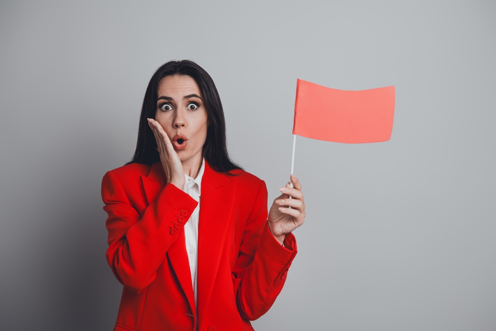 Woman wearing red holding a red flag looking stressed to denote a narcissist