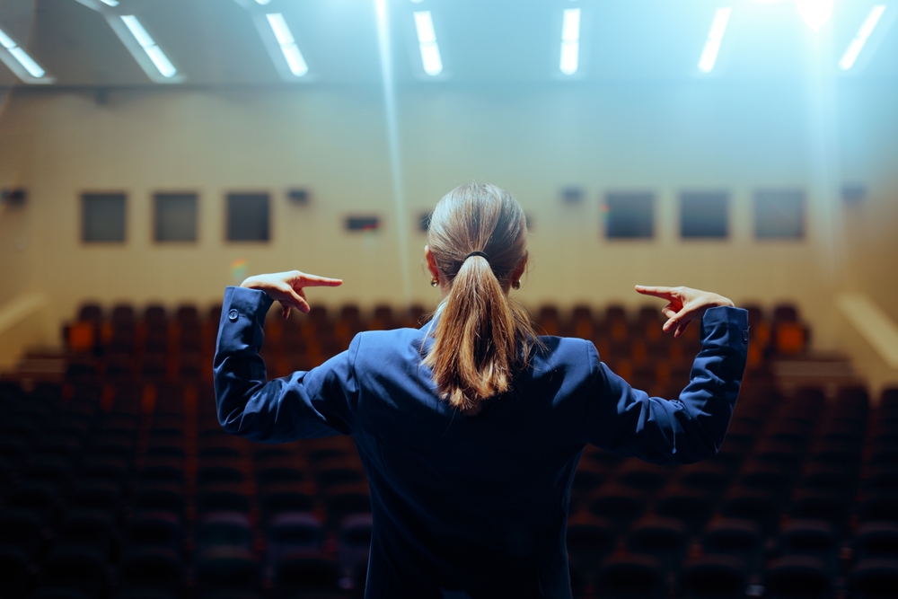 An arrogant and narcissistic leader rehearsing her speech ahead of time in front of an empty hall