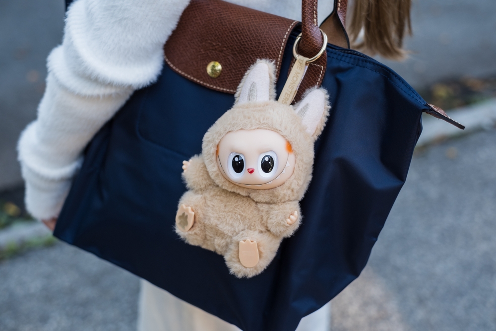 A beige colored labubu doll hanging from a backpack