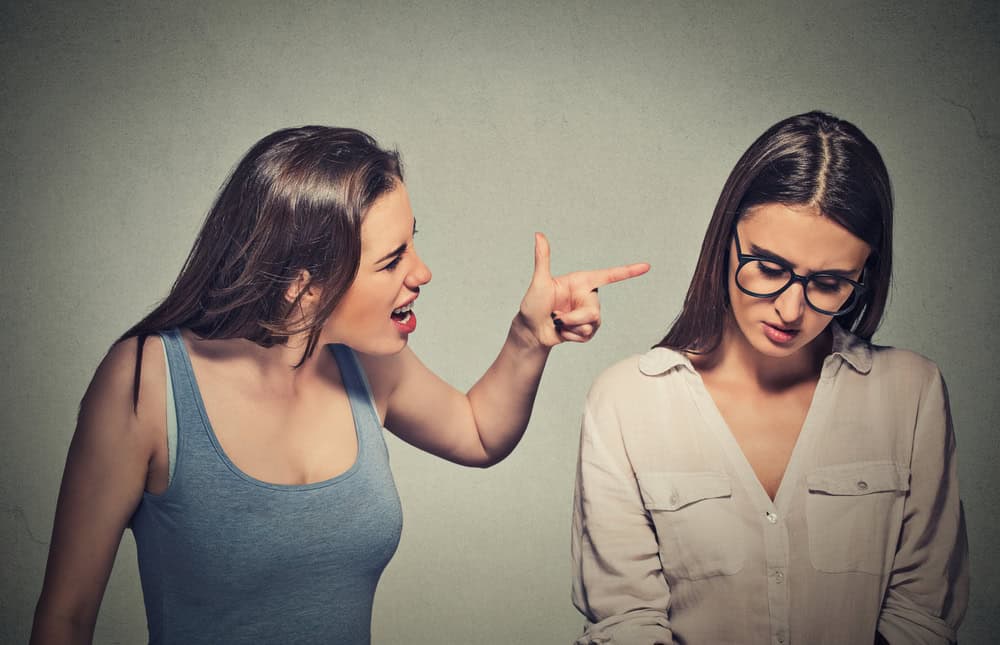 Two female friends standing, one is judging and bullying the other and pointing at her