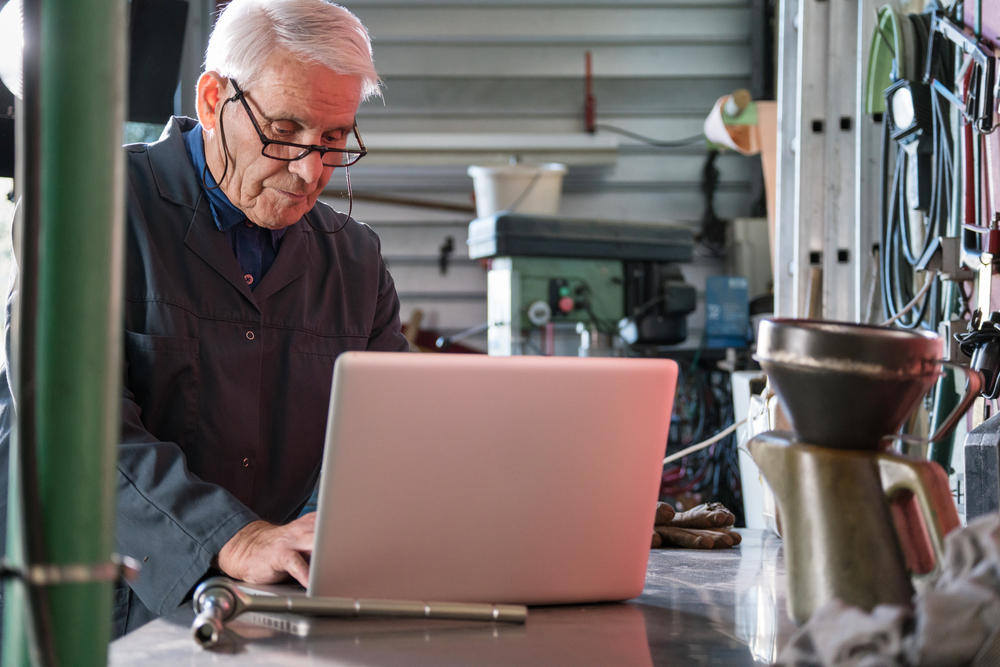 An active gray-haired senior wearing glasses. working on his laptop in his studio