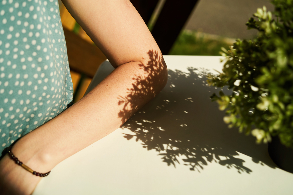 A female's elbow laying on the white table cloth at lunch.