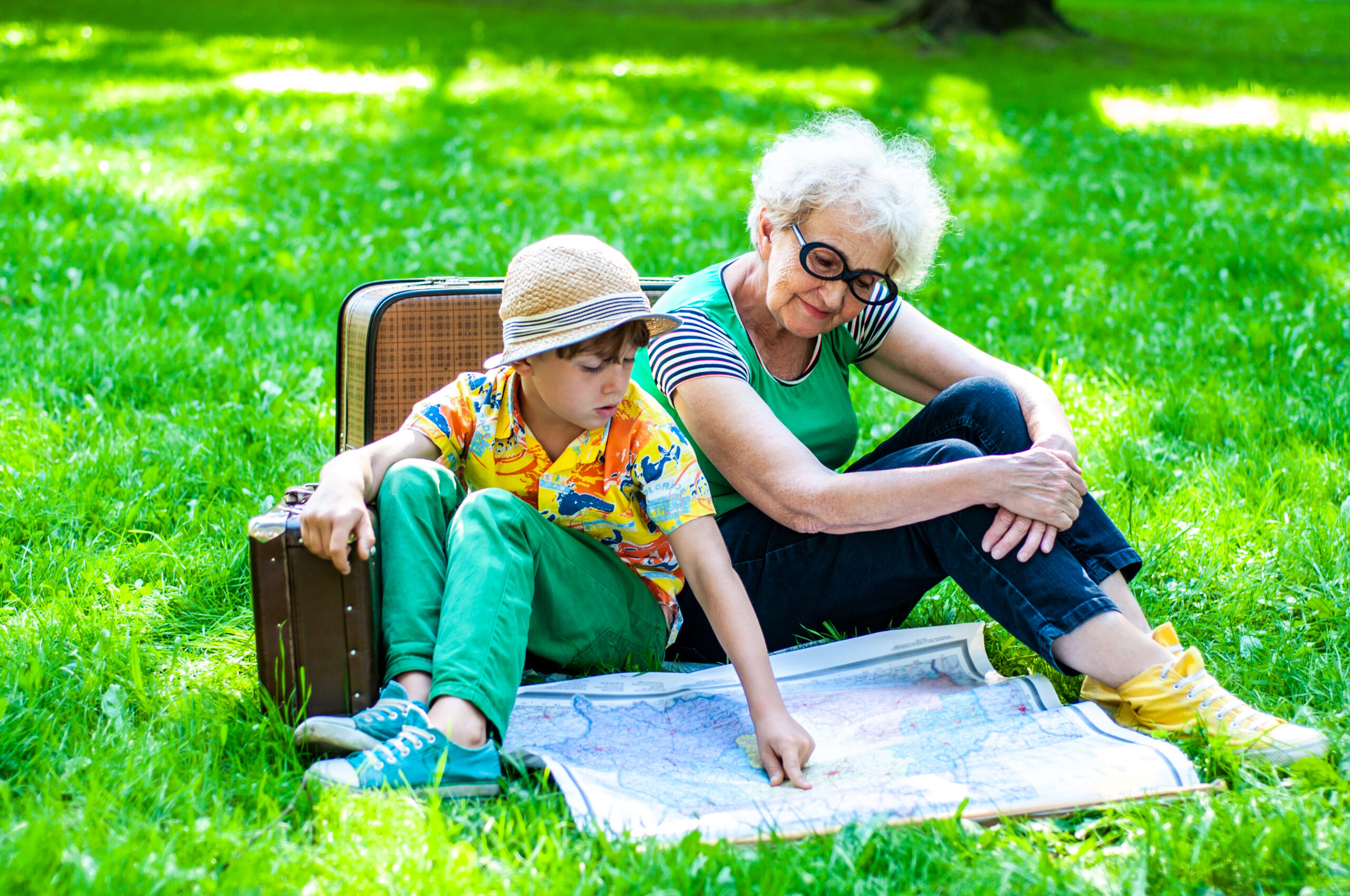 A grandmother sitting in the park with her grandson as they look at a map together.