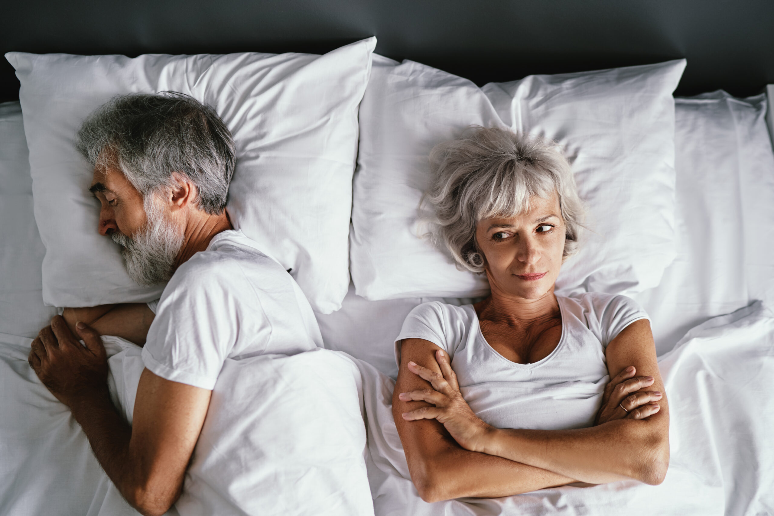 A senior married couple laying in bed.