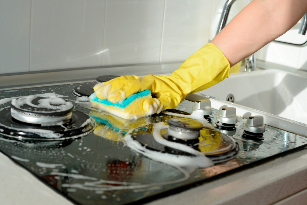 A young woman wearing yellow gloves and cleaning the kitchen stove