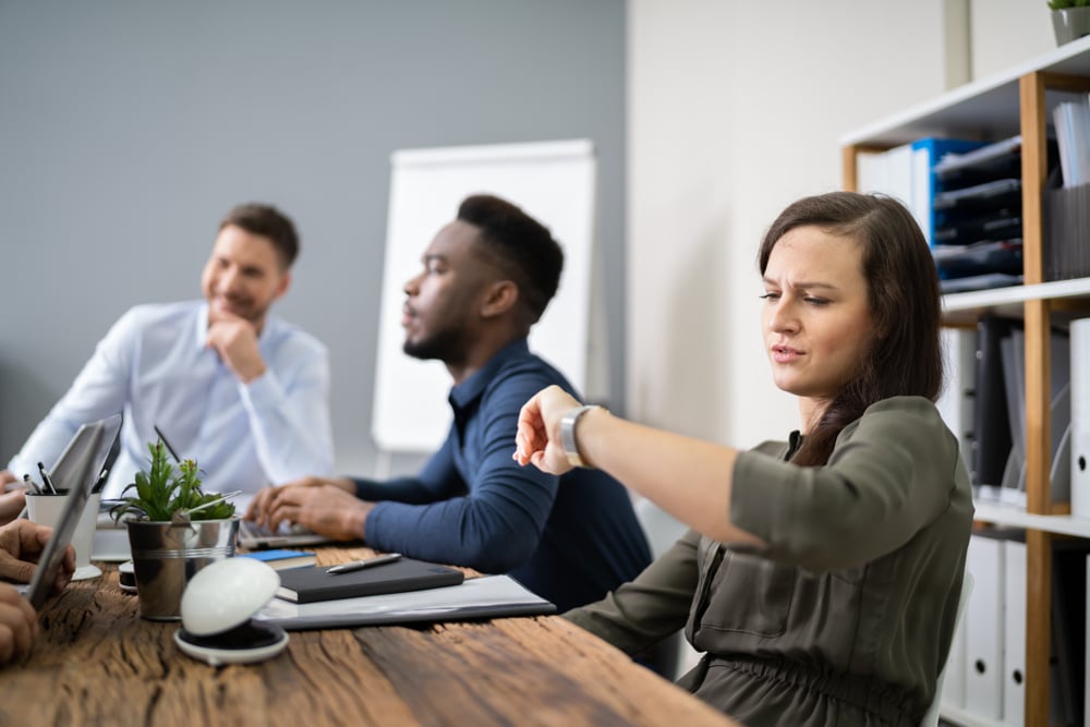 Woman checking time while sitting in a boring meeting with her colleagues