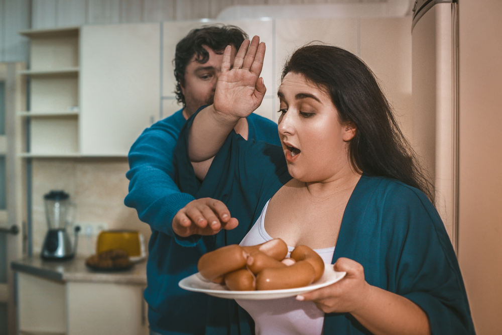 A woman being territorial about her plate forbidding and stopping her husband from grabbing food off her plate