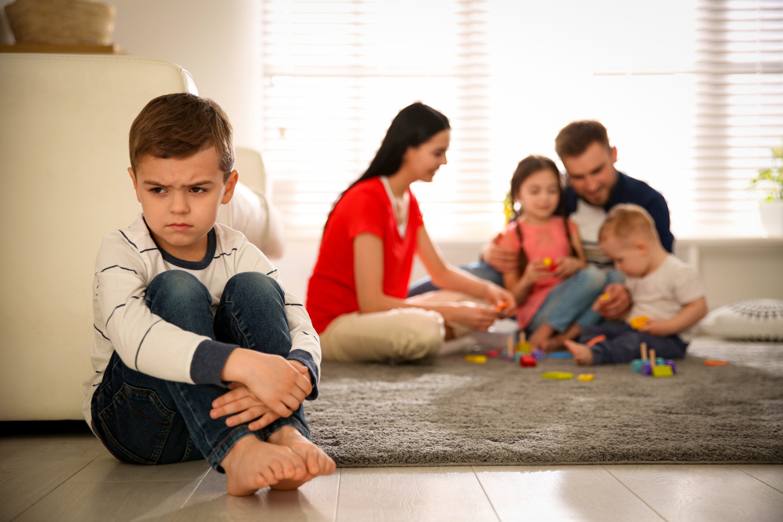 Unhappy little boy feeling ignored while parents spend time with other siblings.