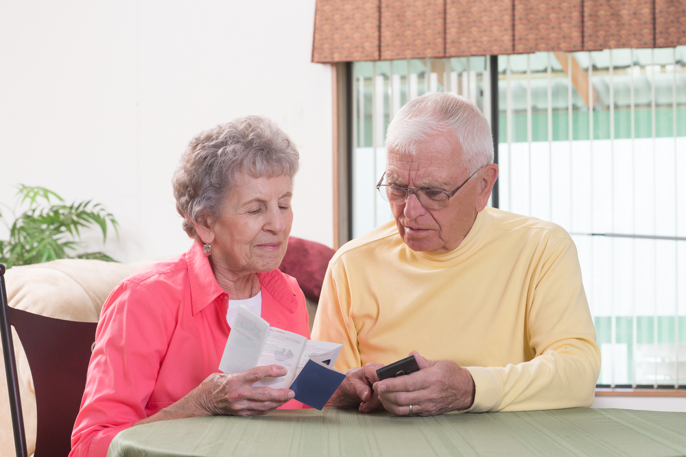 An elderly couple using an instruction manual as they try to use a cell phone