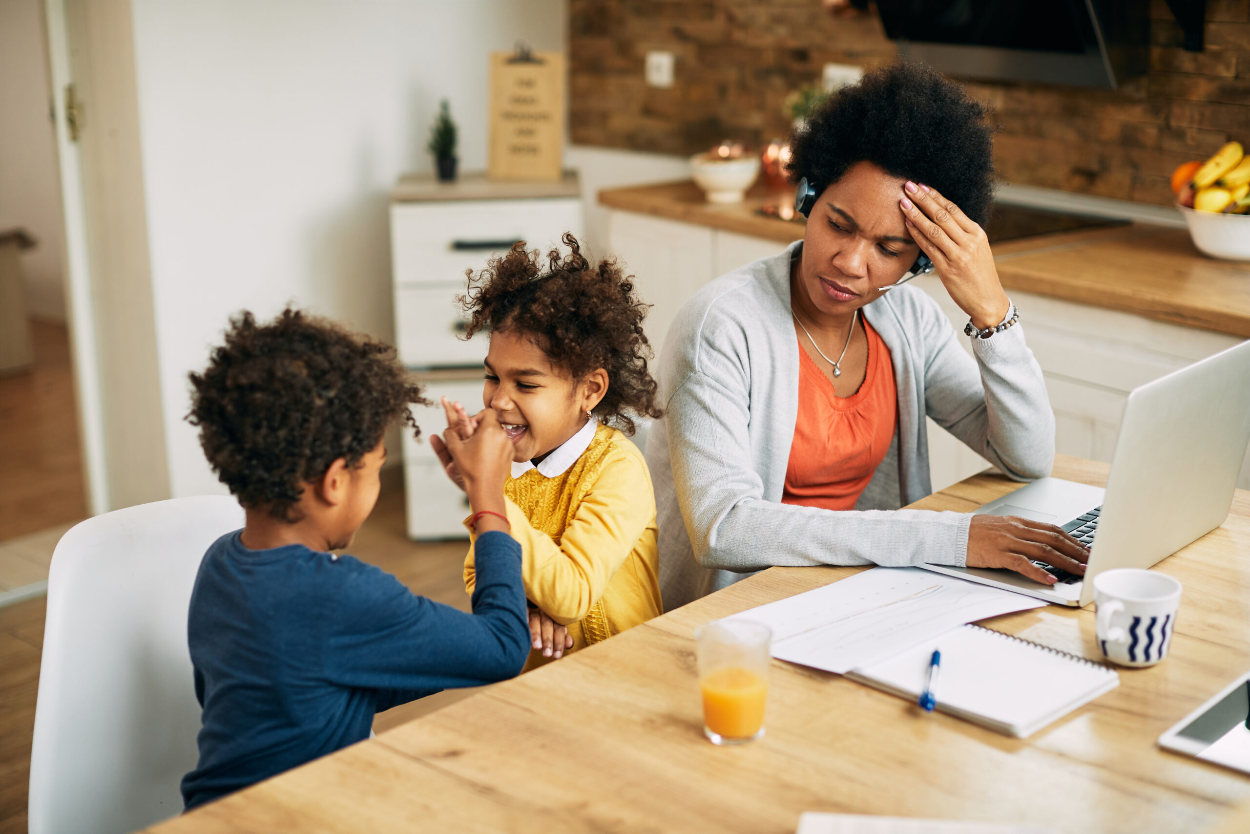 A frustrated young mother busy with work while her children play nearby.
