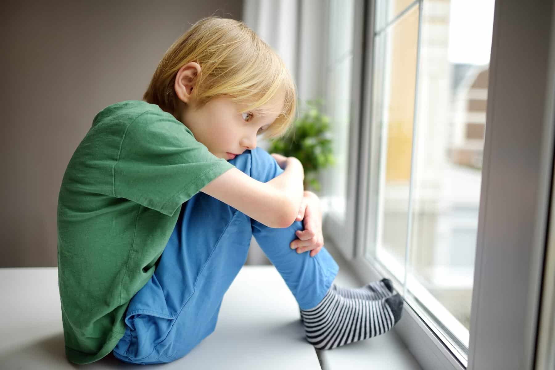 A sad and lonely little boy looking out the window.