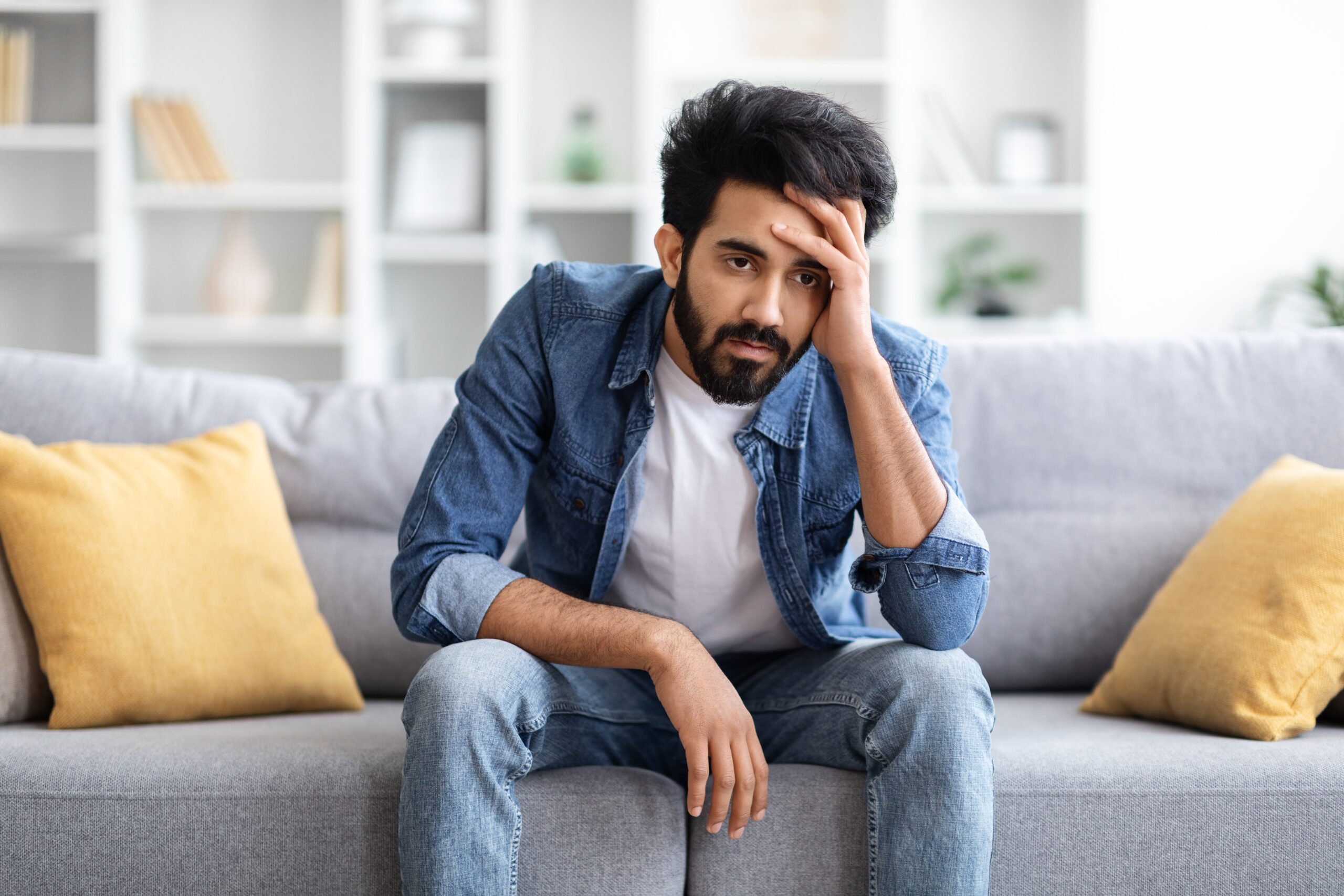 A dissatisfied man at home with his head in his hand.
