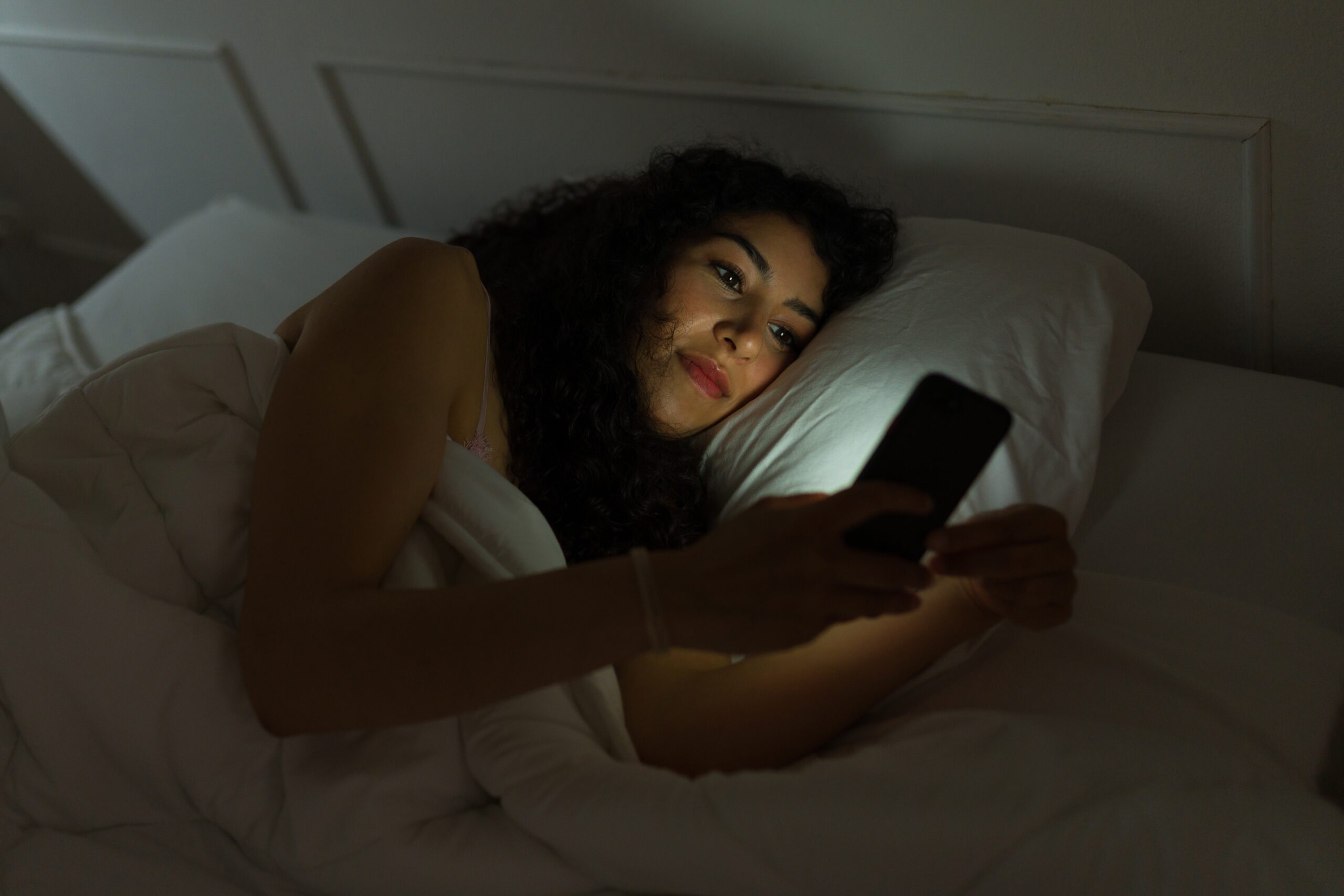 A woman laying awake at night scrolling on her phone.