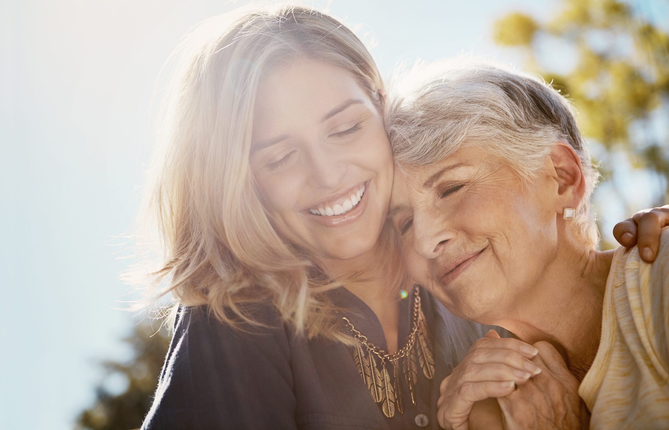 A woman hugging her adult daughter and smiling.