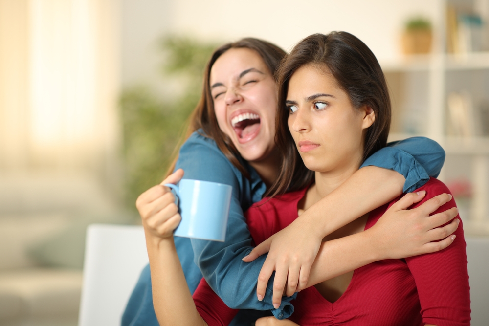 A woman uncomfortable with physical affection and hugs being hugged by her excited and affectionate friend
