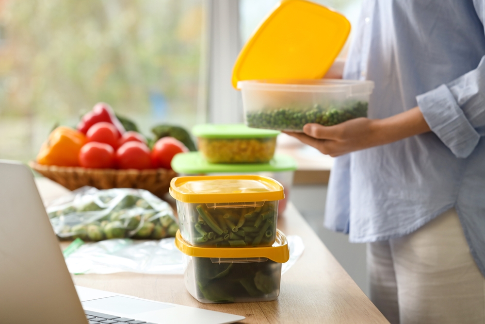 A woman with tupperwares containers containing veggies, and packing veggies into other plastic containers