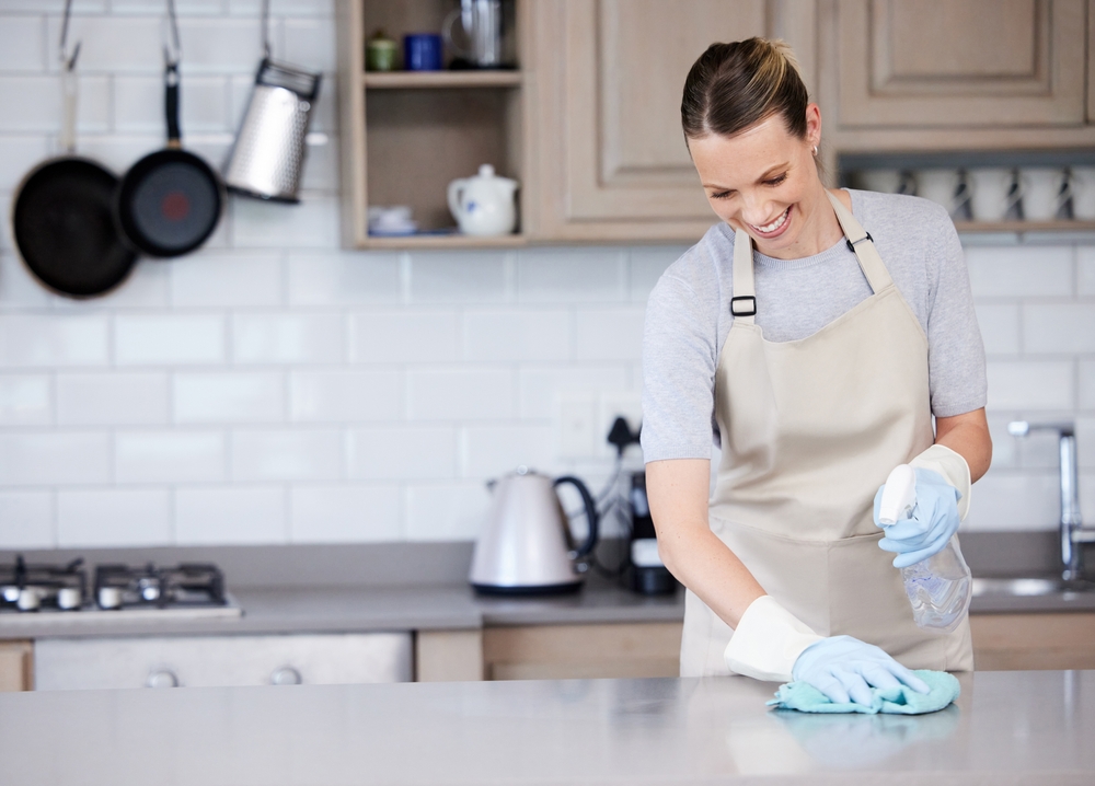 A woman wearing white rubber gloves and cleaning the kitchen