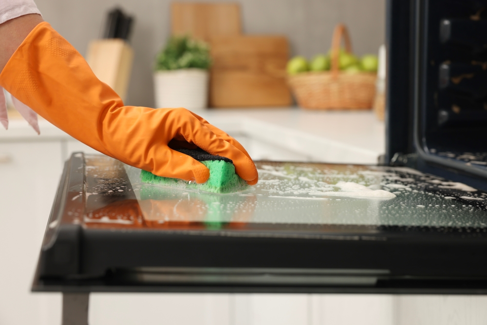 A hand in orange rubber gloves cleaning the kitchen.