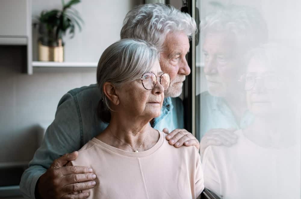 Senior couple wistfully looking out the window together.