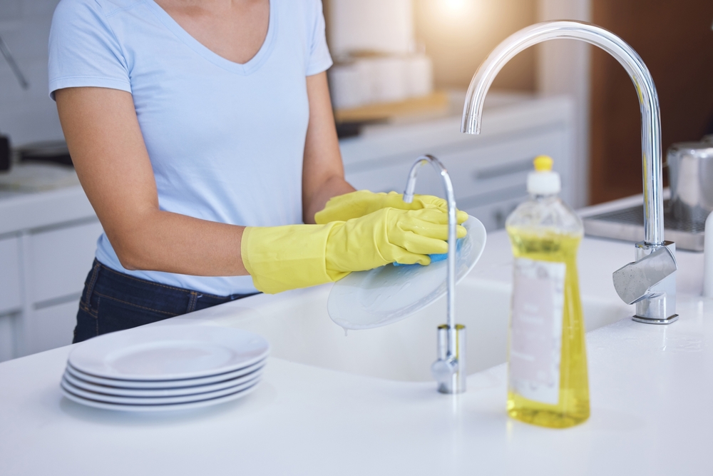 A woman in yellow rubber gloves washing dishes in the kitchen