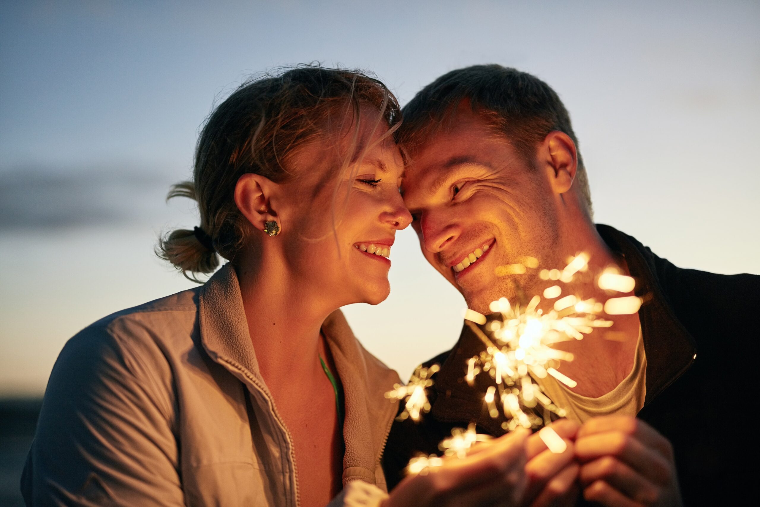 Couple looking at each other romantically while holding a sparkler.