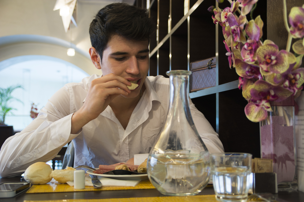 An elegant young man eating bread at his dinning table