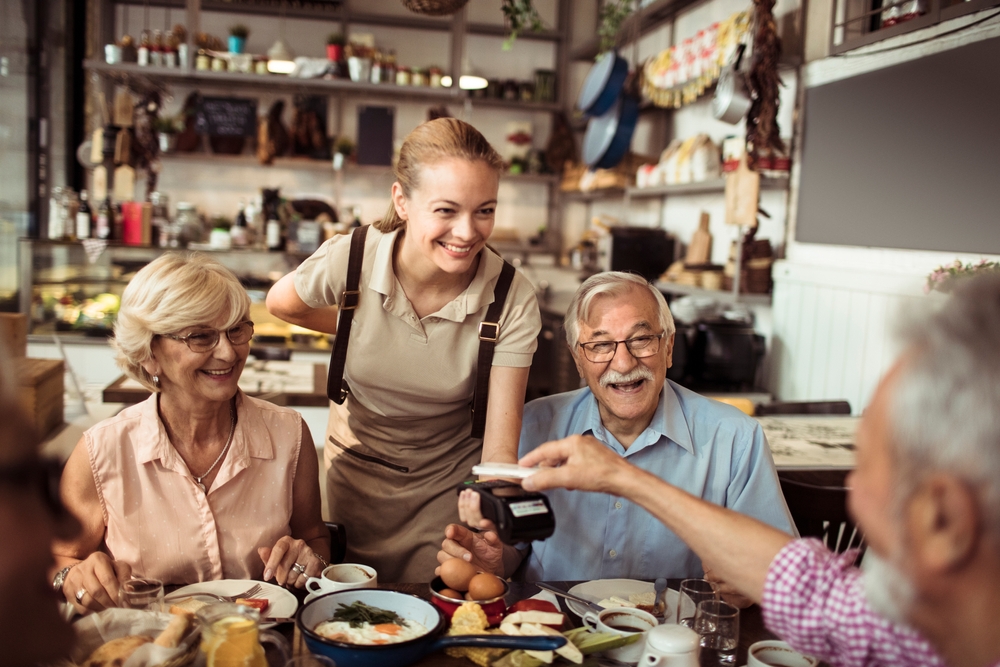 A senior man paying the dinner bill while out with his senior friends