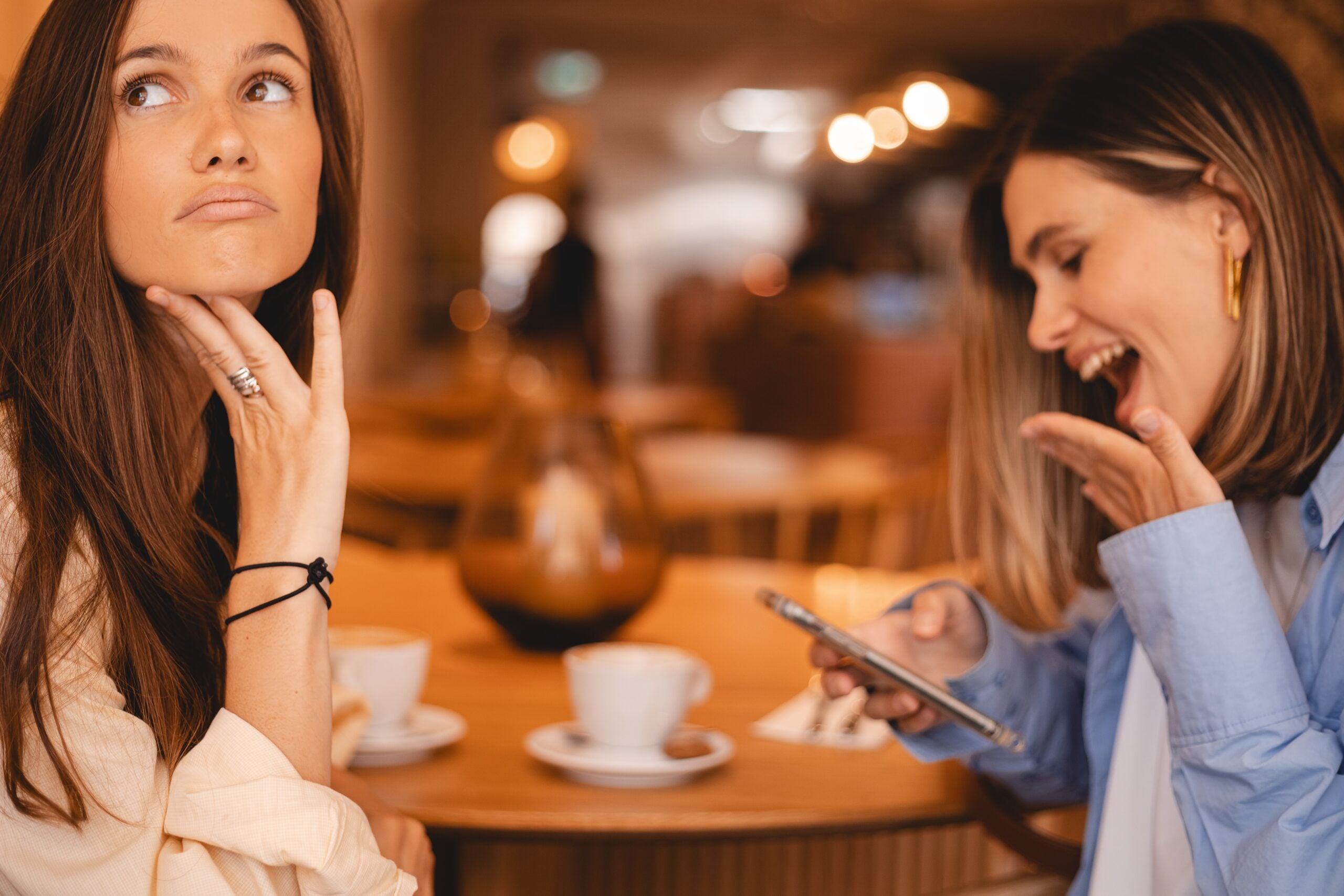 Two girlfriends sitting together at a cafe with not much to discuss.