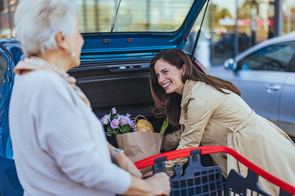 A smiling young woman helping an elderly woman load her groceries into the car