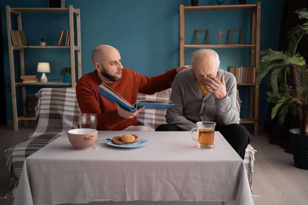 An elderly senior father and adult son sitting on the sofa at home together and looking at pictures.
