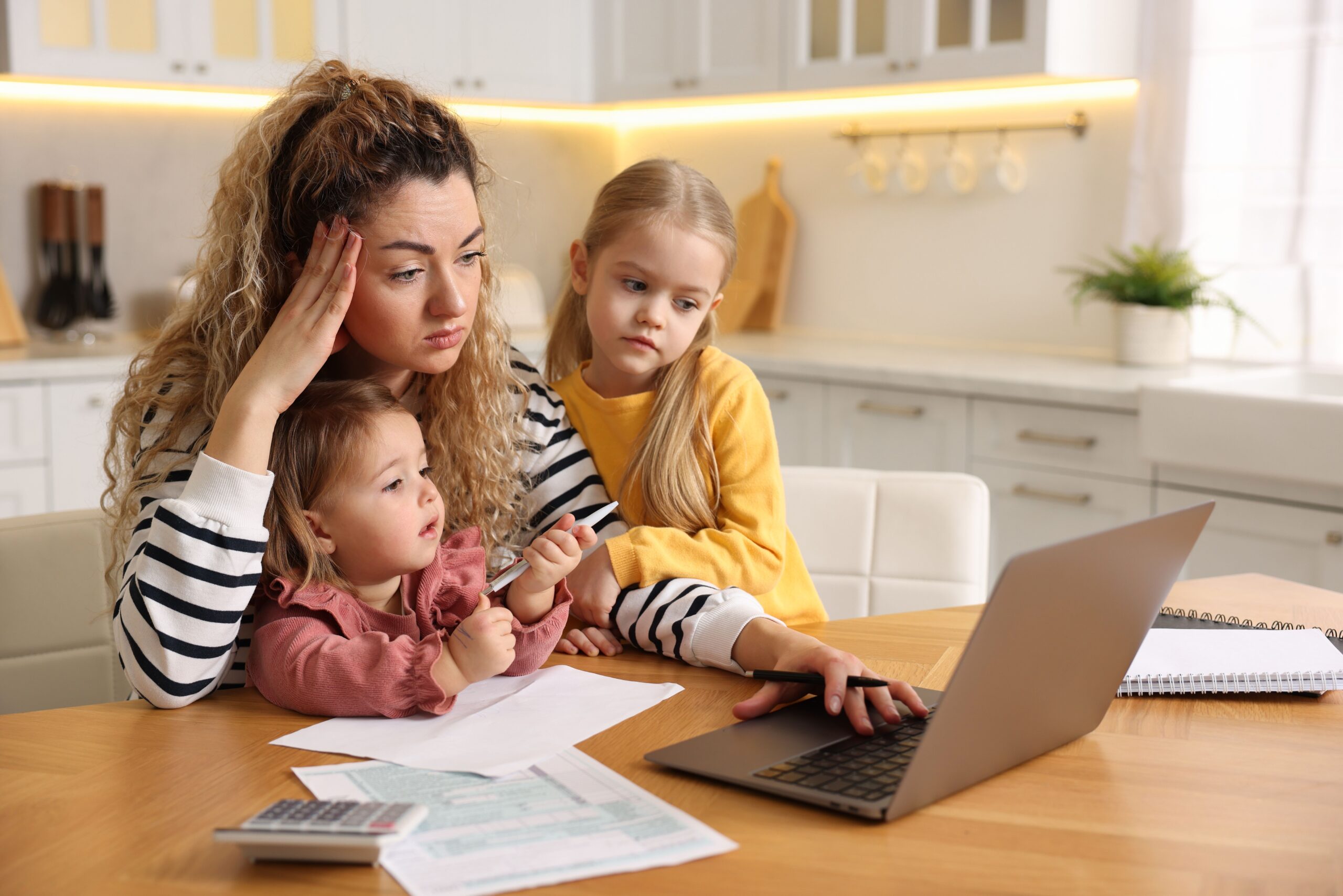 An overwhelmed mother doing paperwork while with her children.