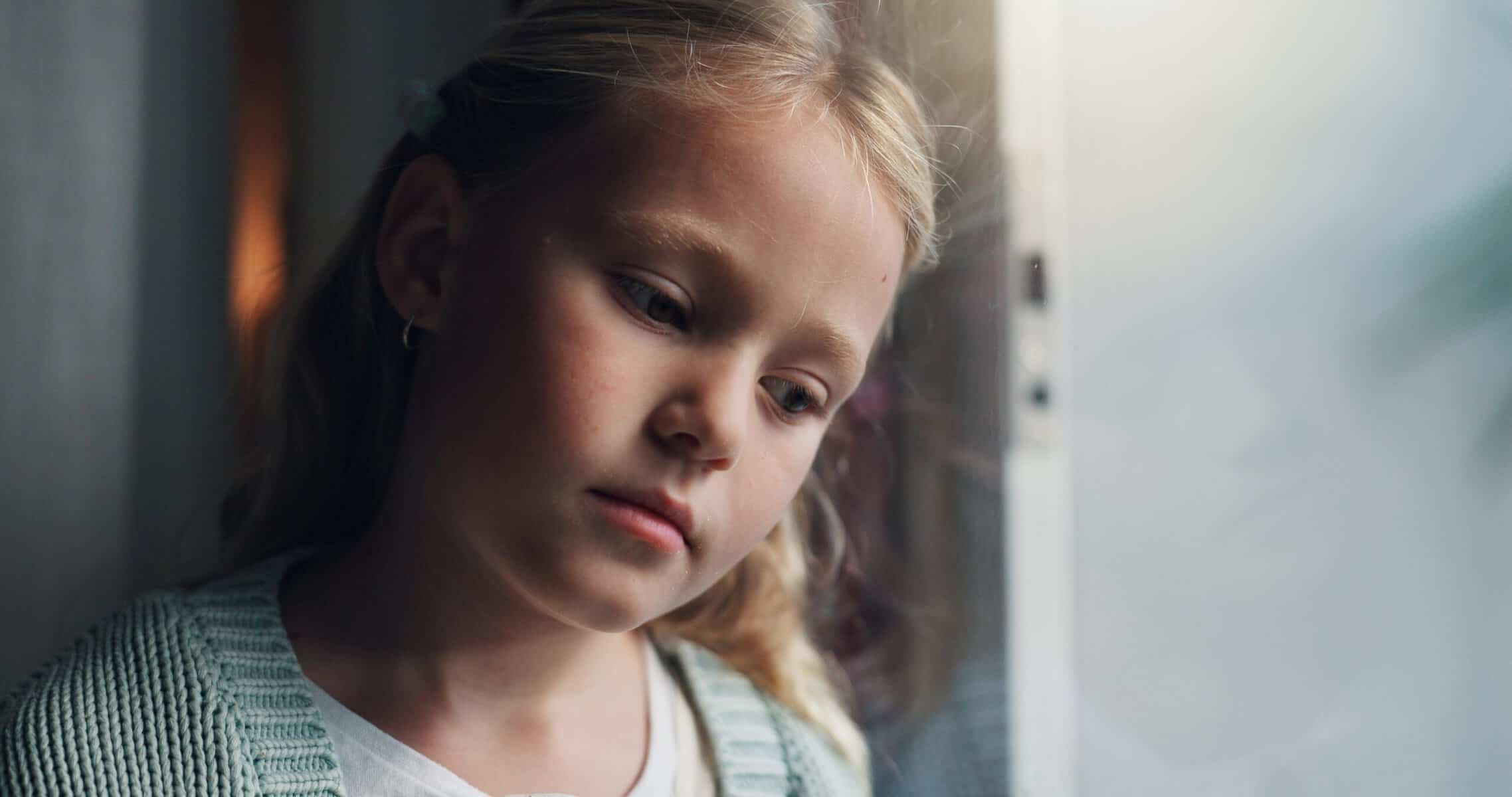 A lonely little girl looking sadly out of a window.
