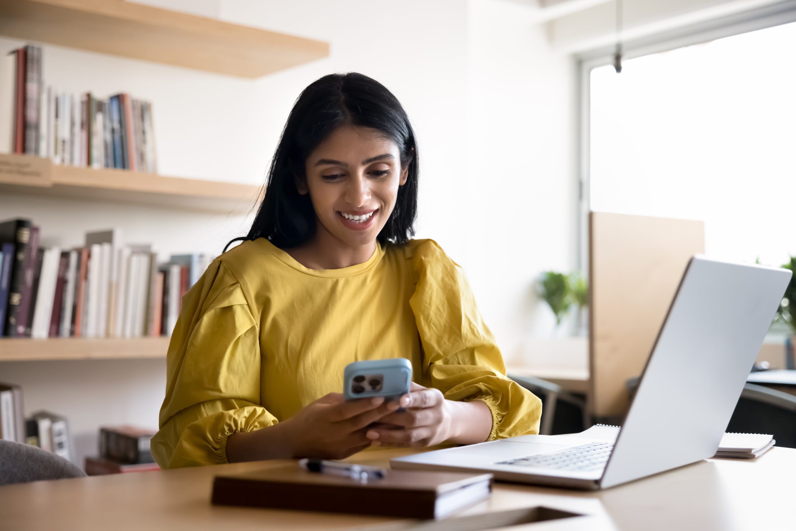 A smiling woman reading emails at her desk.