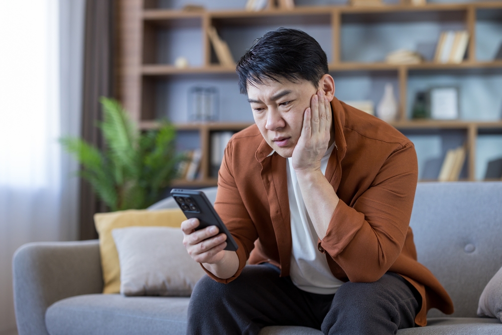 An Asian middle aged man sitting in the living room and using his phone