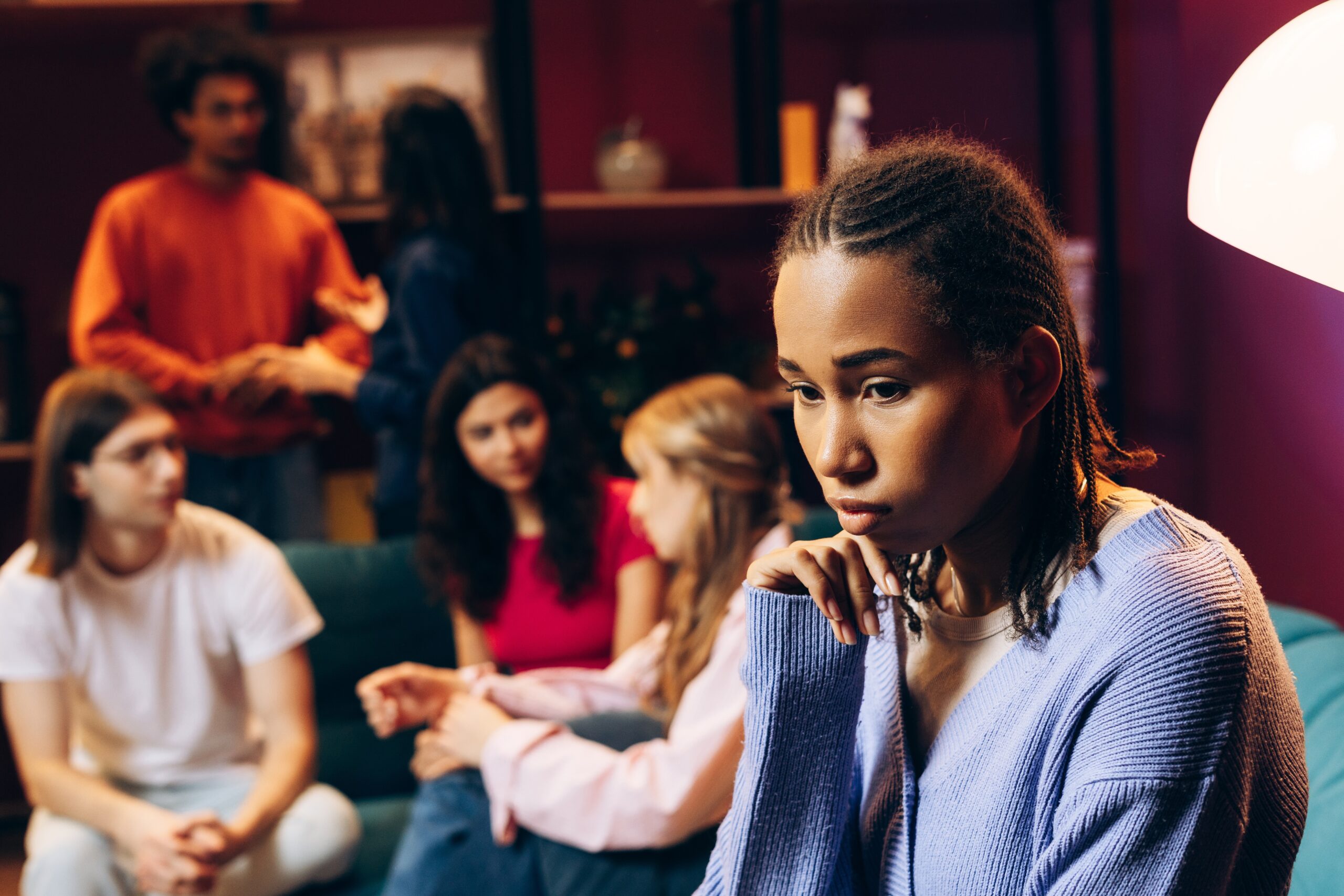 Young woman sitting alone at a party with friends.